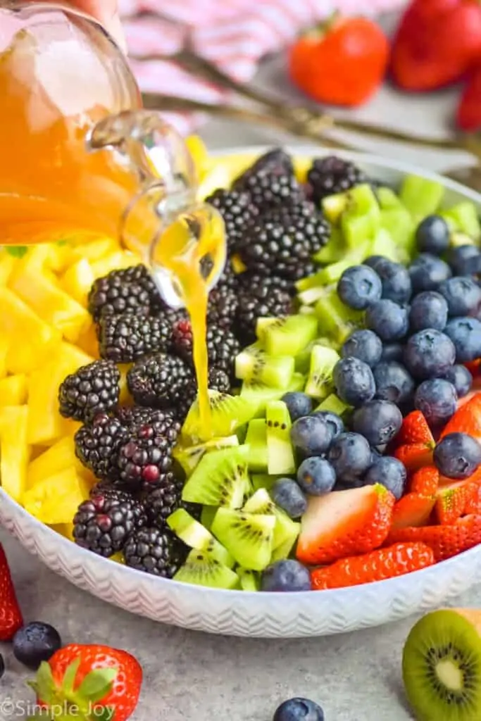 fruit salad dressing being poured over fruit in a bowl