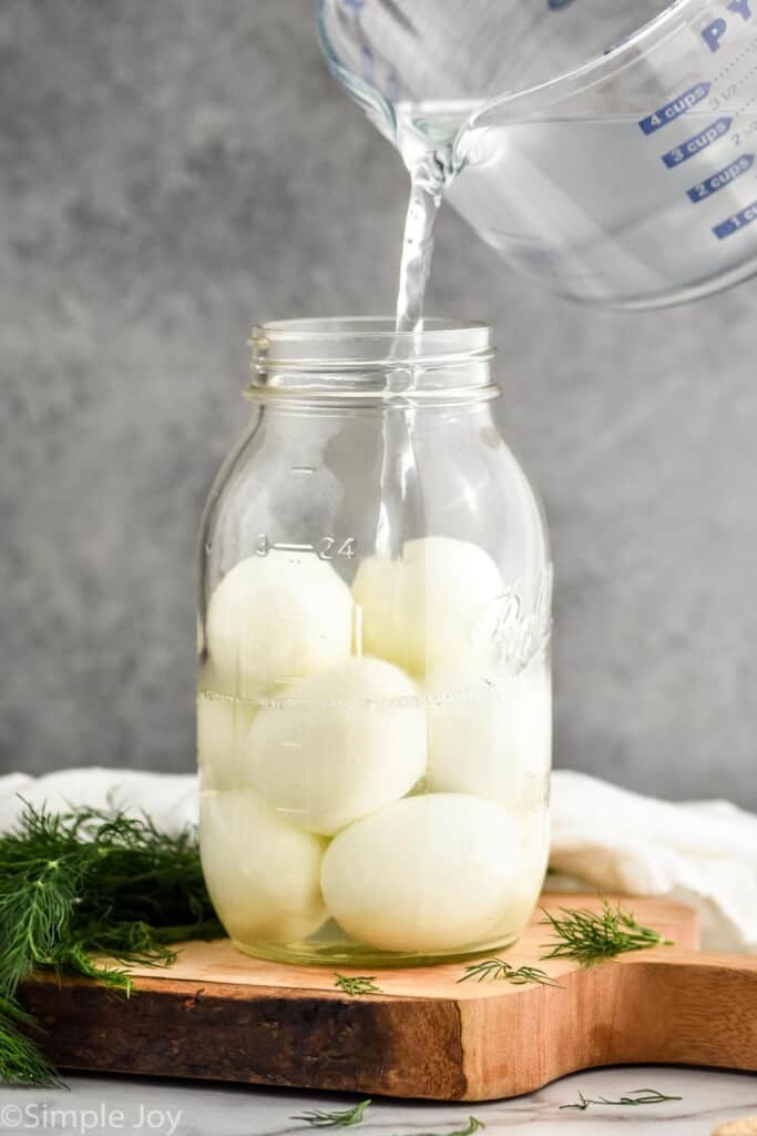 pouring brining mixture into a mason jar that has hard boiled eggs in it