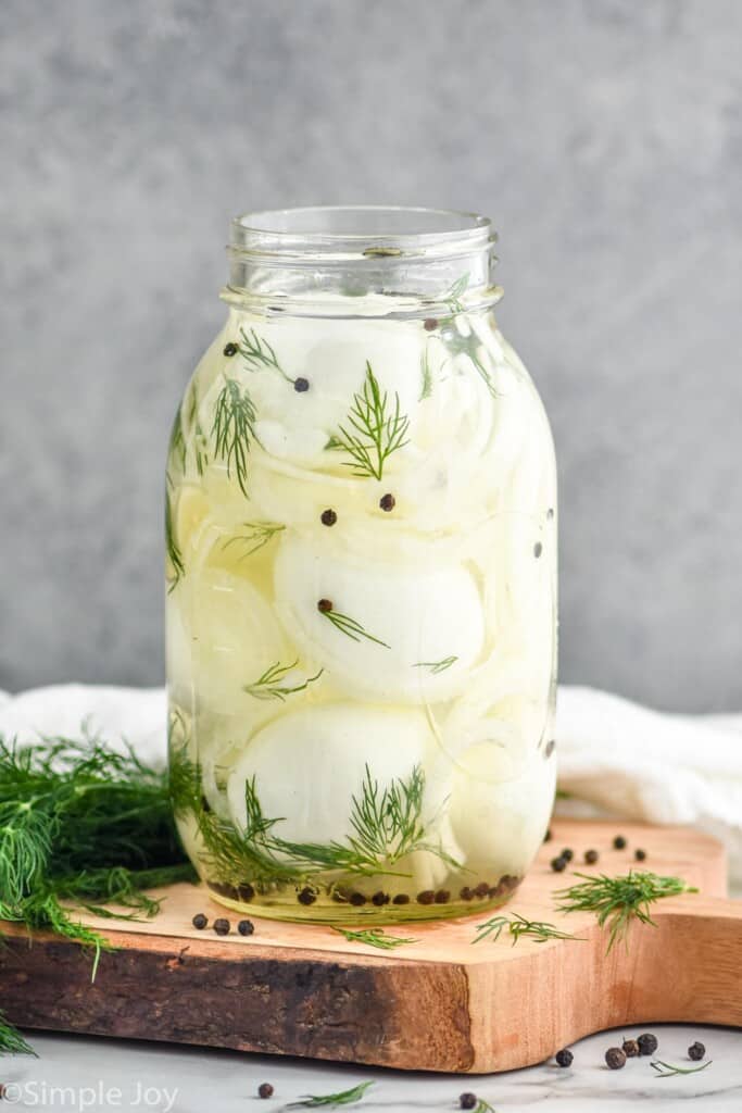 a jar of hard boiled eggs with liquid, peppercorns, and fresh dill