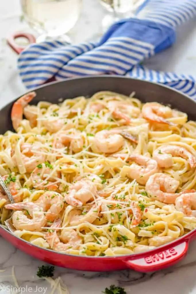 side view of a red skillet full of shrimp pasta recipe garnished with parmesan and parsley