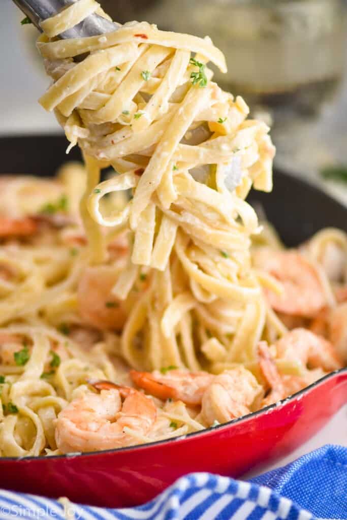 creamy fettuccine noodles being pulled out of a skillet with shrimp and pasta in it