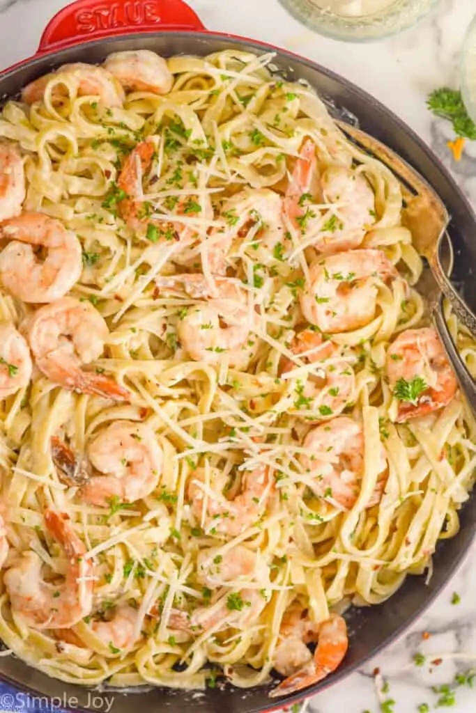 overhead of a skillet full of shrimp pasta garnished with parsley and parmesan