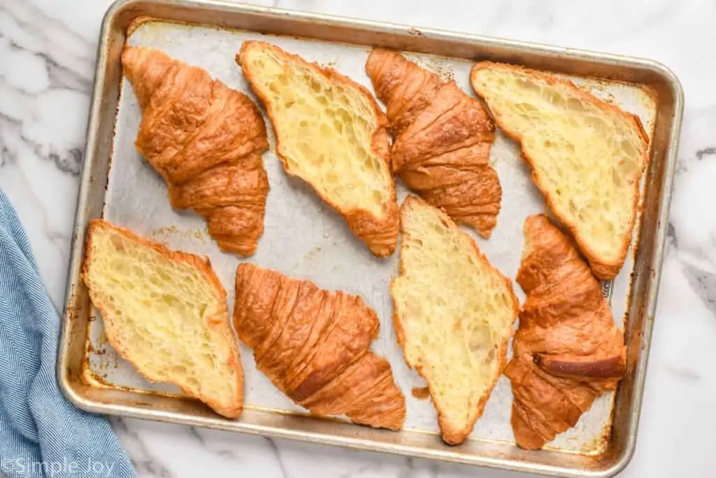 four croissants that have been cut in half and placed on a rimmed baking sheet