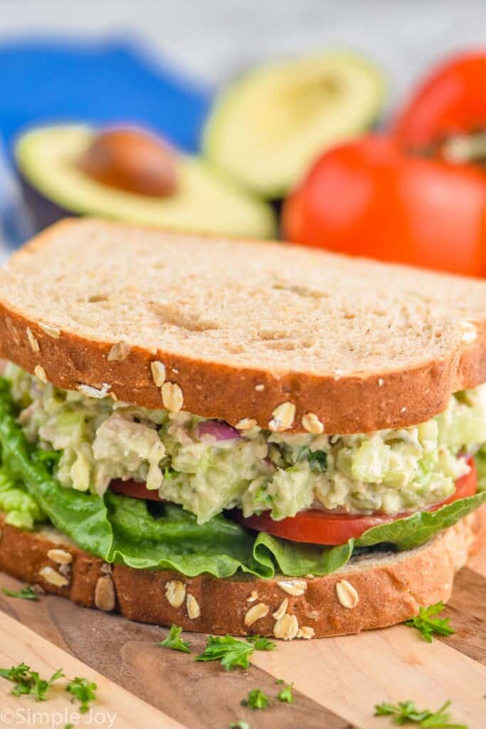 an avocado tuna salad sandwich with tomato and lettuce on a cutting board