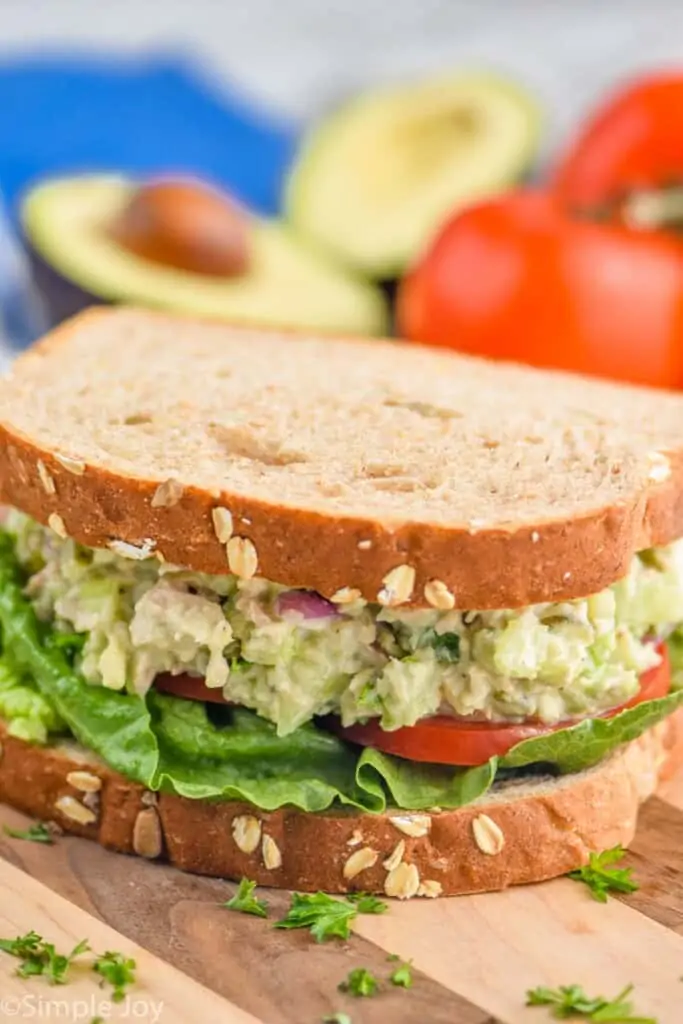 an avocado tuna salad sandwich with tomato and lettuce on a cutting board