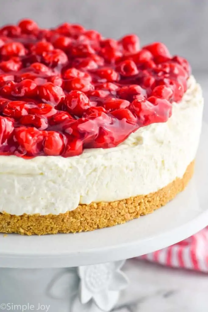 close up of a cheesecake topped with cherries on a cake stand