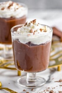 a small goblet holding chocolate pudding with whipped cream and chocolate shavings