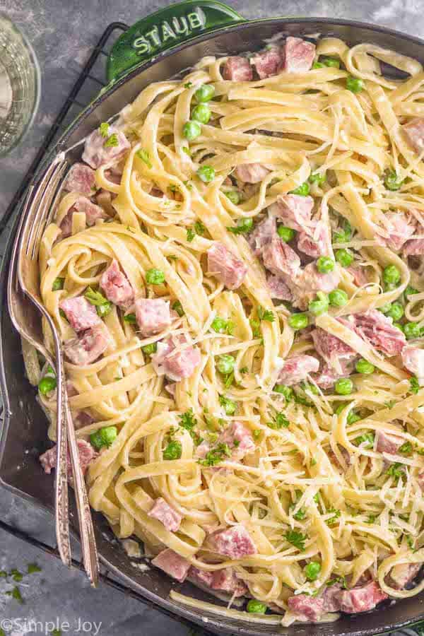 overhead close up view of ham and pea pasta in a skillet garnished with freshly grated parmesan cheese