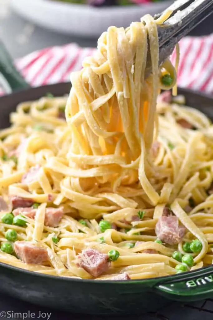 tongs lifting creamy fettuccine noodles out of a skillet