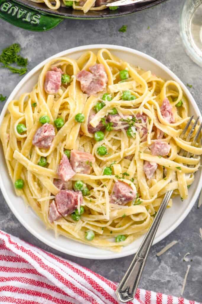 overhead of a white plate filled with noodles, ham, and peas