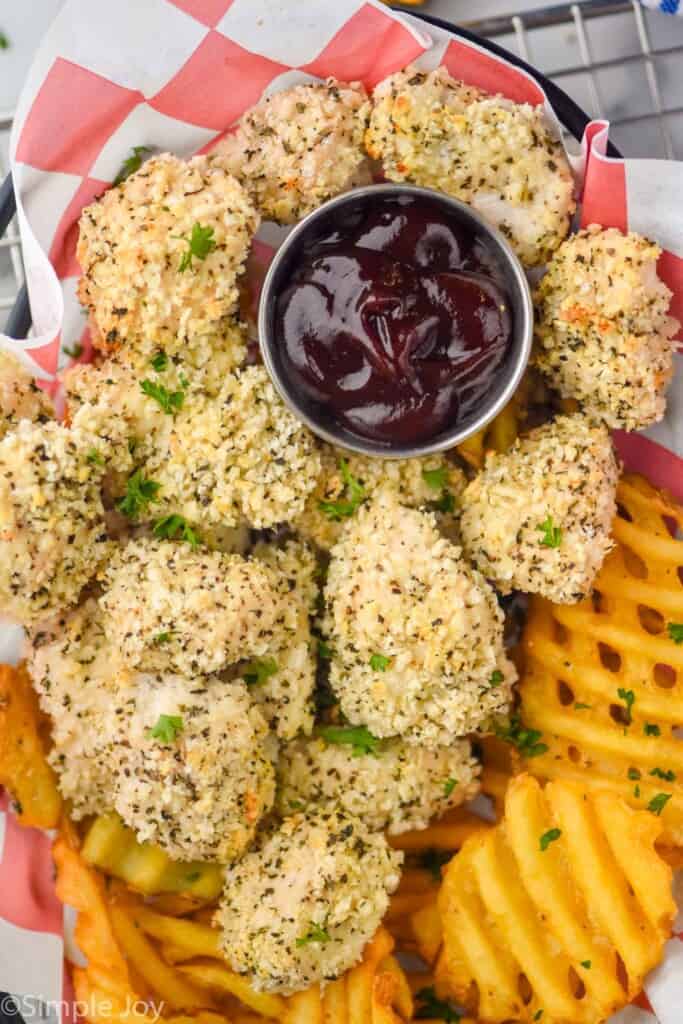 close up of homemade chicken nuggets in a basket with a small dish of bbq sauce and fries