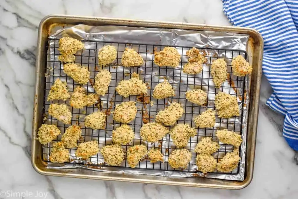 overhead of rimmed baking sheet lined with aluminum foil and cooling rack with chicken nuggets on it