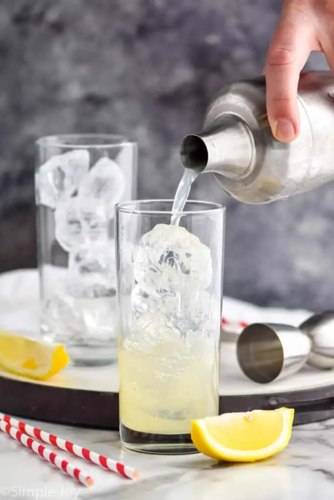 pouring mixed alcohol into a high ball glass filled with ice