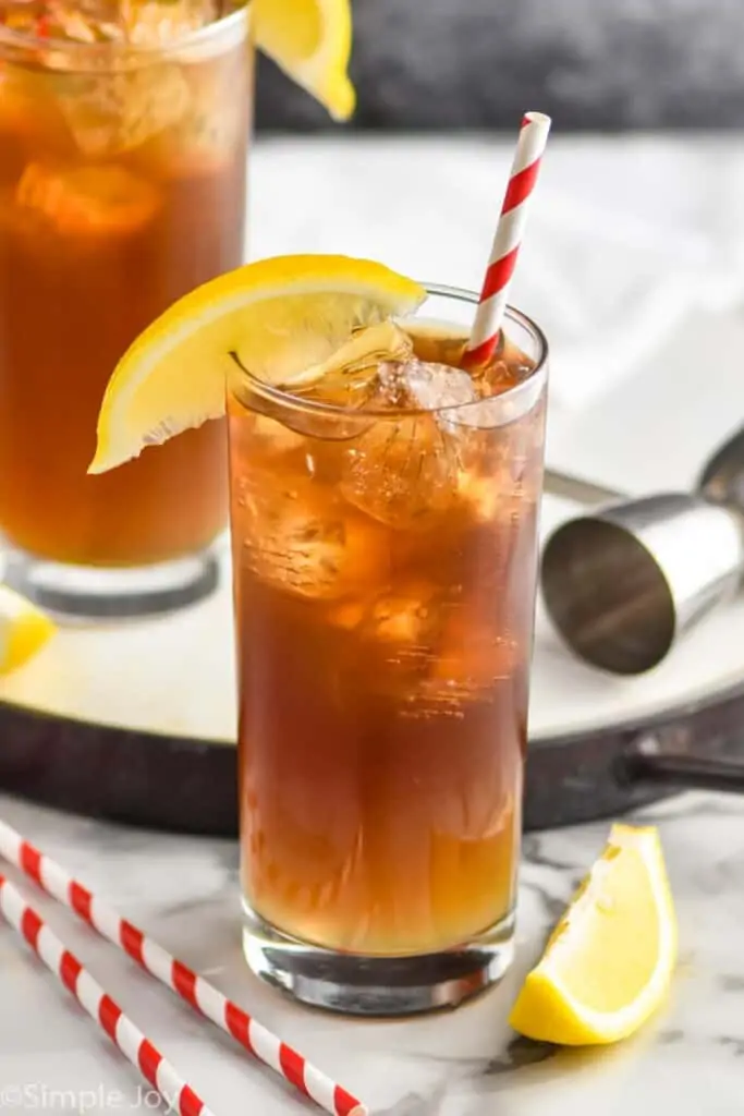 high ball glass garnished with a lemon wedge and dark cocktail