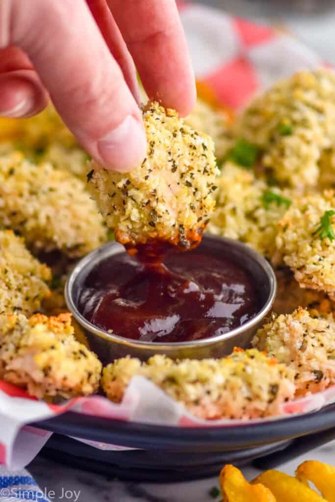 close up of a parmesan chicken nugget being dipped in BBQ sauce