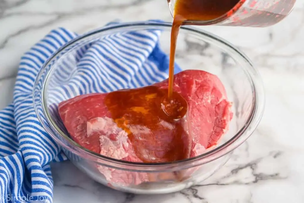 marinade being poured over a large piece of beef