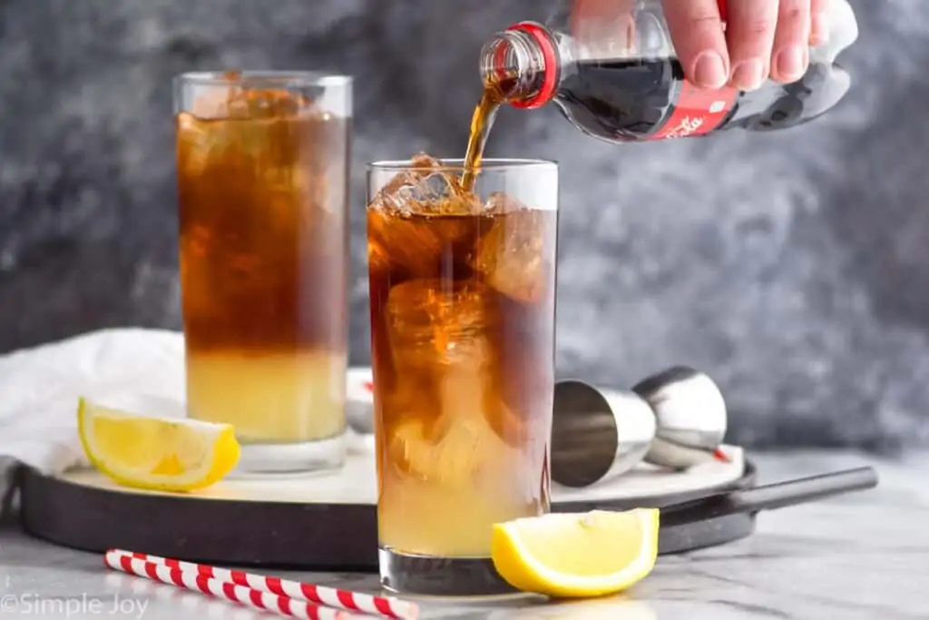pouring coke into a high ball glass filled with ice and mixed alcohol