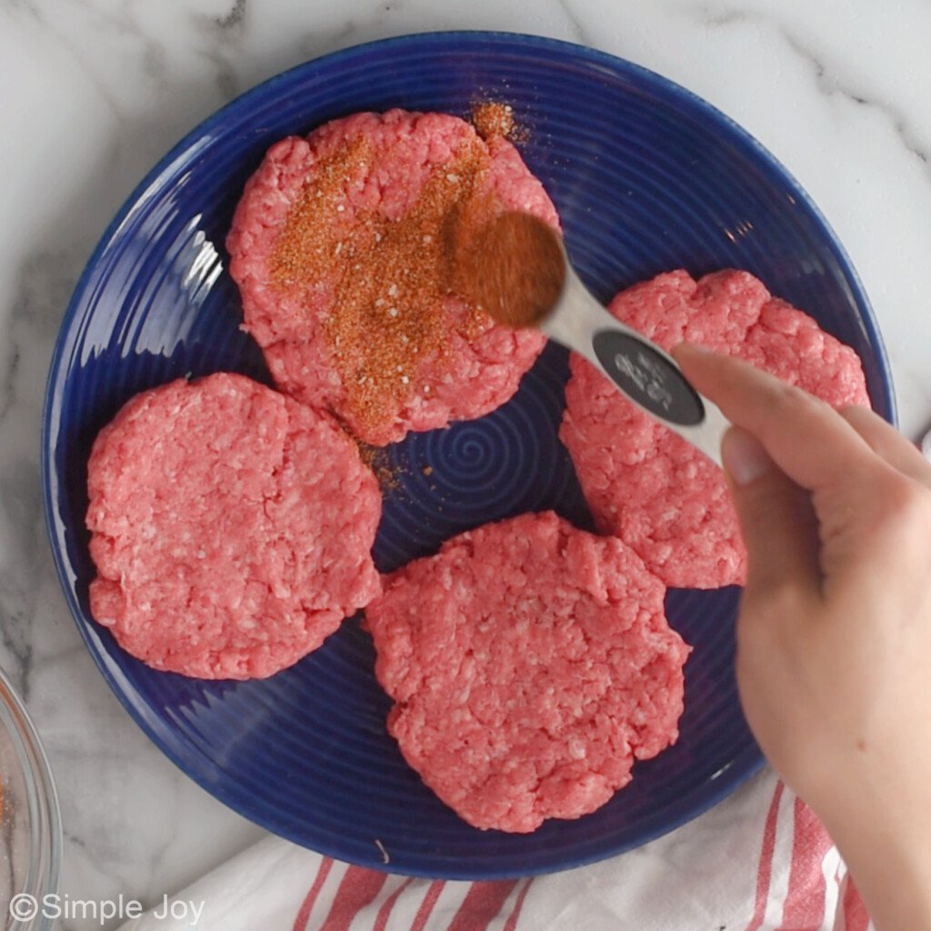adding burger seasoning to formed uncooked burger patties