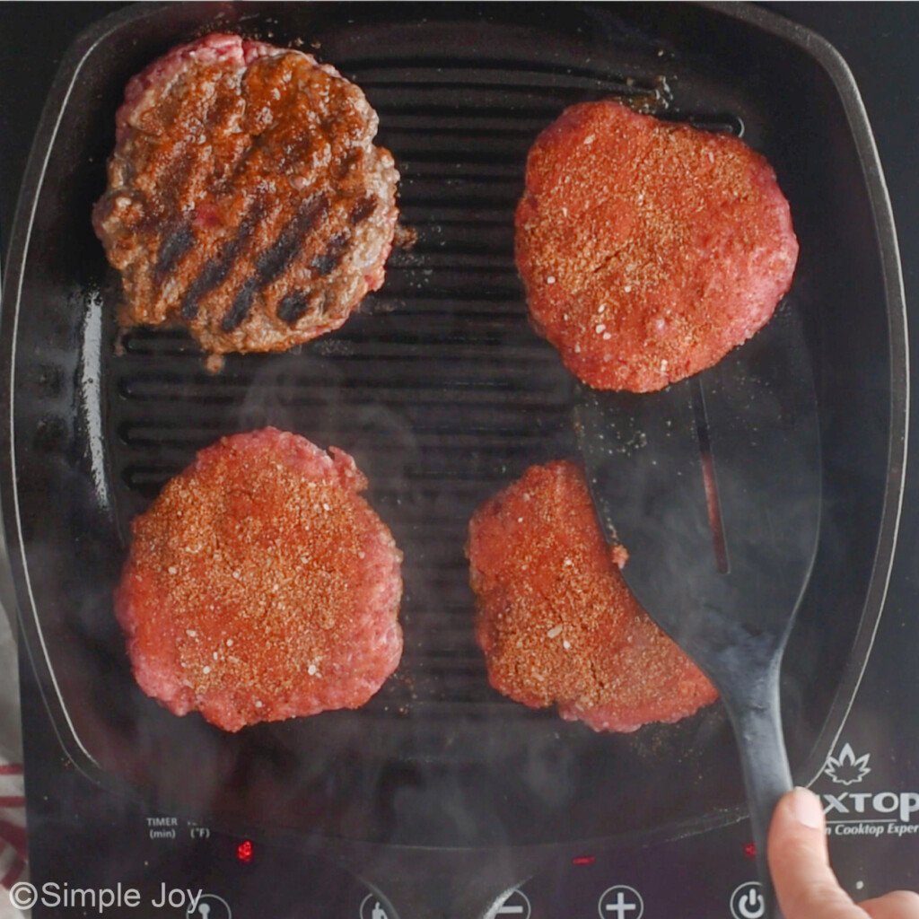 four seasoned burger patties being cooked