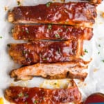 pinterest graphic of a row of slow cooker bbq ribs after being cooked, cut up on parchment paper with extra bbq sauce