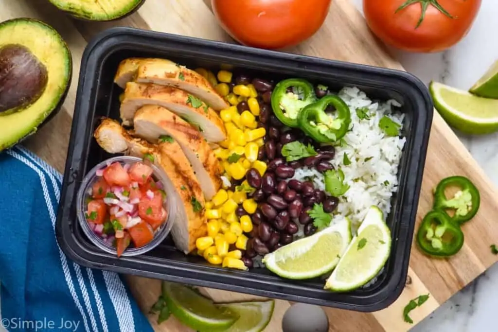 overhead of burrito bowl in a meal prep container with rice, beans, corn, chicken, and Pico de Gallo in a small cup