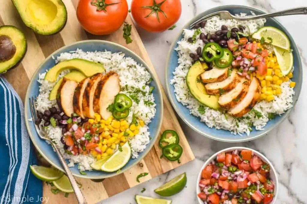 overhead of two chicken burrito bowls that have rice, corn, chicken, pico, avocado, and jalapeños