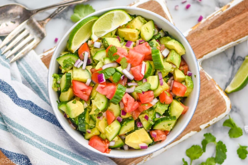 overhead of cucumber and avocado salad in a large bowl, garnished with two lime wedges
