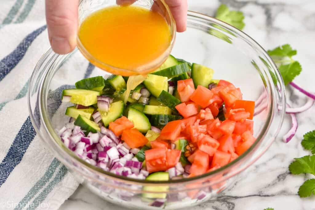 dressing being poured over cucumber avocado salad