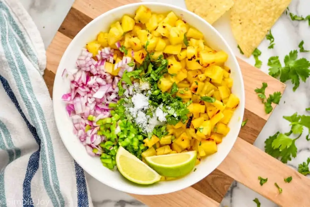 overhead of a white bowl with ingredients for grilled pineapple salsa separated out