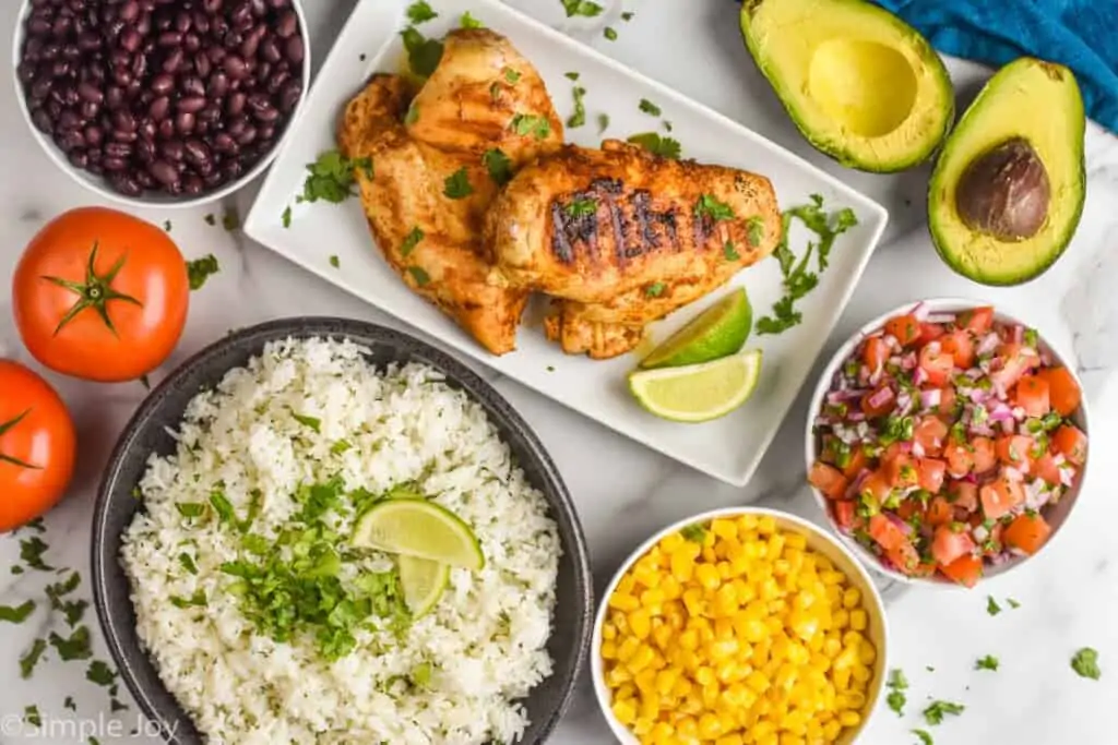 overhead of cilantro lime rice, corn, Pico de Gallo, beans, and grilled chicken in plates and bowls