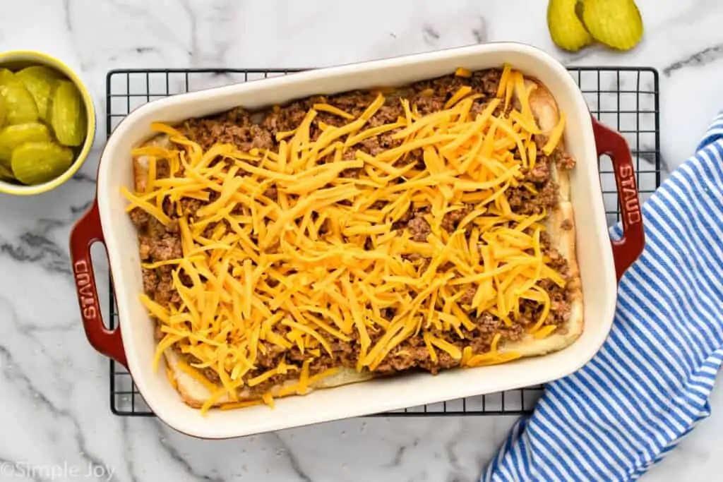 overhead of a baking dish that has the bottom of rolls, ground beef, and shredded cheddar cheese