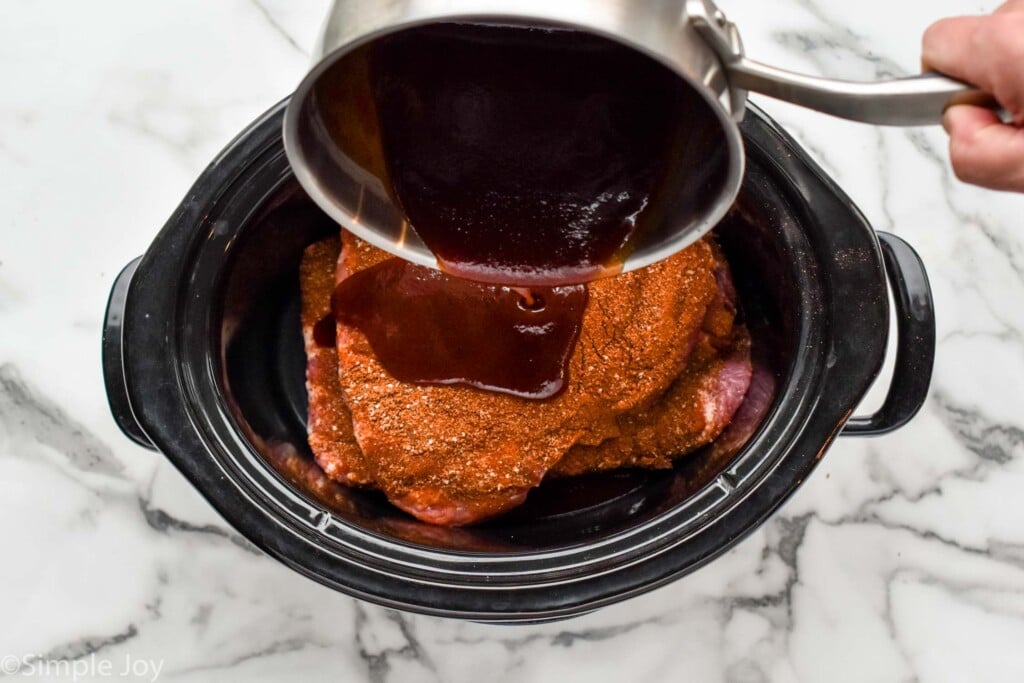 pouring a little bbq sauce over a second layer of uncooked ribs in a slow cooker