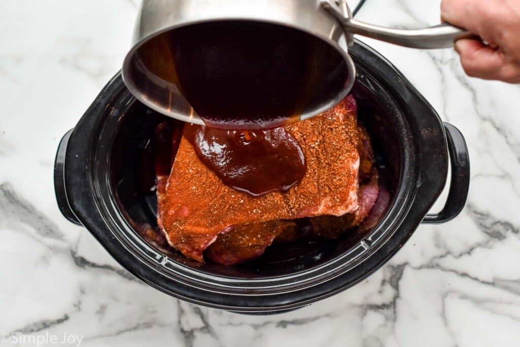 pouring a little bbq sauce over a third layer of uncooked ribs in a slow cooker