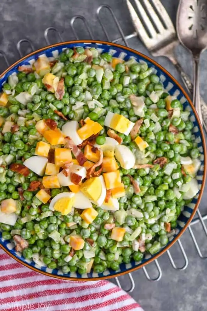 overhead of pea salad in a serving bowl with extra cheese, egg, and bacon on top