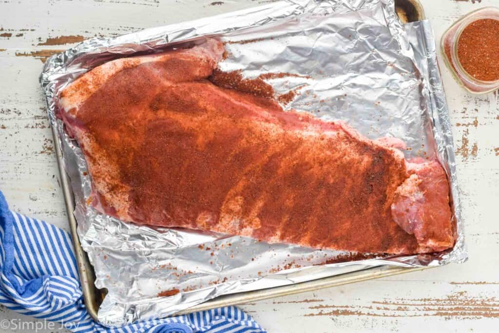 overhead of a rack of ribs with pork rub on them on a foil lined baking sheet