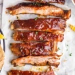 a row of slow cooker bbq ribs after being cooked, cut up on parchment paper with extra bbq sauce - 27