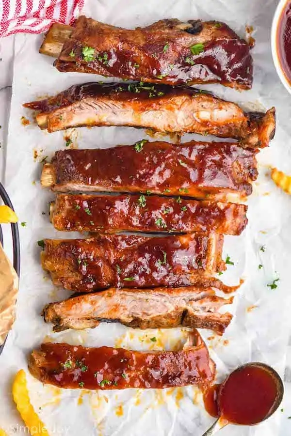 a row of slow cooker bbq ribs after being cooked, cut up on parchment paper with extra bbq sauce