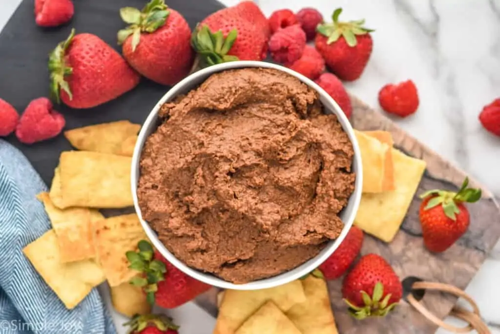overhead of a bowl of chocolate humus on a platter with chips and berries