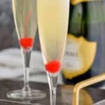 two champagne flutes with cherries at the bottom of them holding a French 76