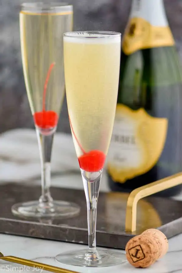 two champagne flutes with cherries at the bottom of them holding a French 76