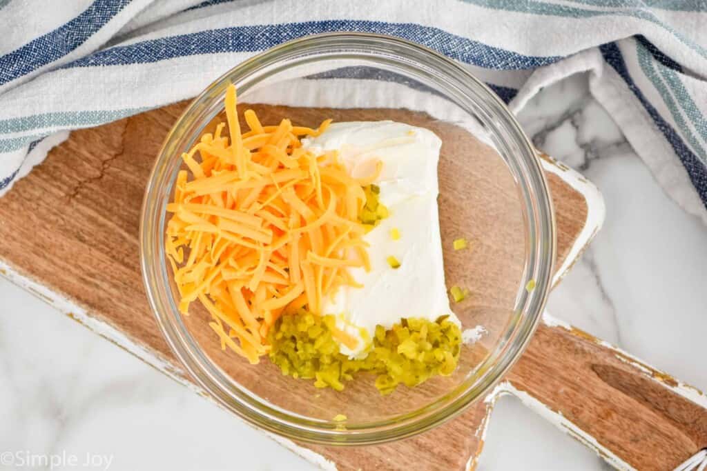 overhead of a bowl with a brick of cream cheese, shredded cheese, and pickle relish