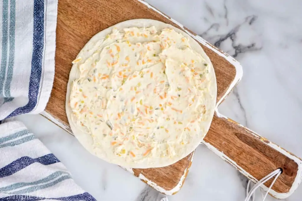 a tortilla on a cutting board with cream cheese mixture on it