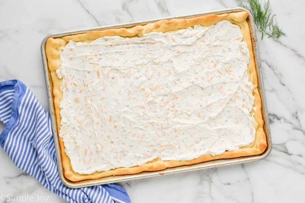 crescent roll dough in a baking sheet with cream cheese and sour cream mixture spread over it