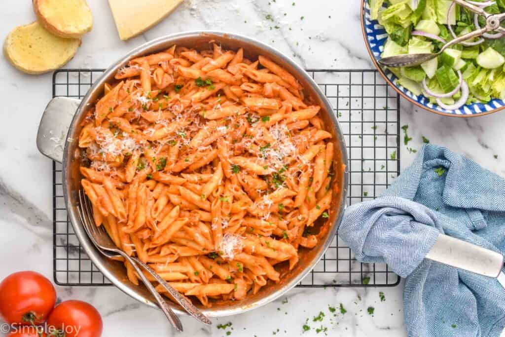 overhead of a skillet full of penne Alla vodka on a cooling rack with a salad next to it