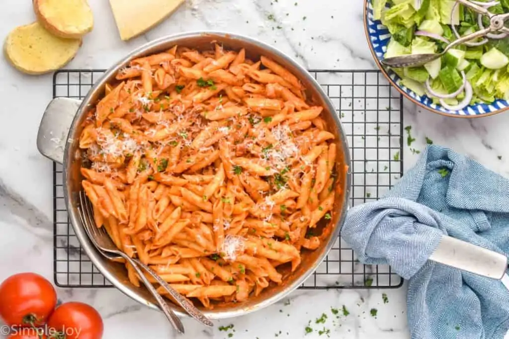 overhead of a skillet full of penne Alla vodka on a cooling rack with a salad next to it