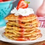 a stack of strawberry pancakes topped with whipped cream and half a strawberry