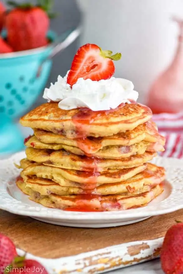 a stack of strawberry pancakes topped with whipped cream and half a strawberry