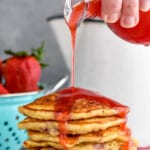 strawberry syrup being poured on a pile of strawberry pancakes