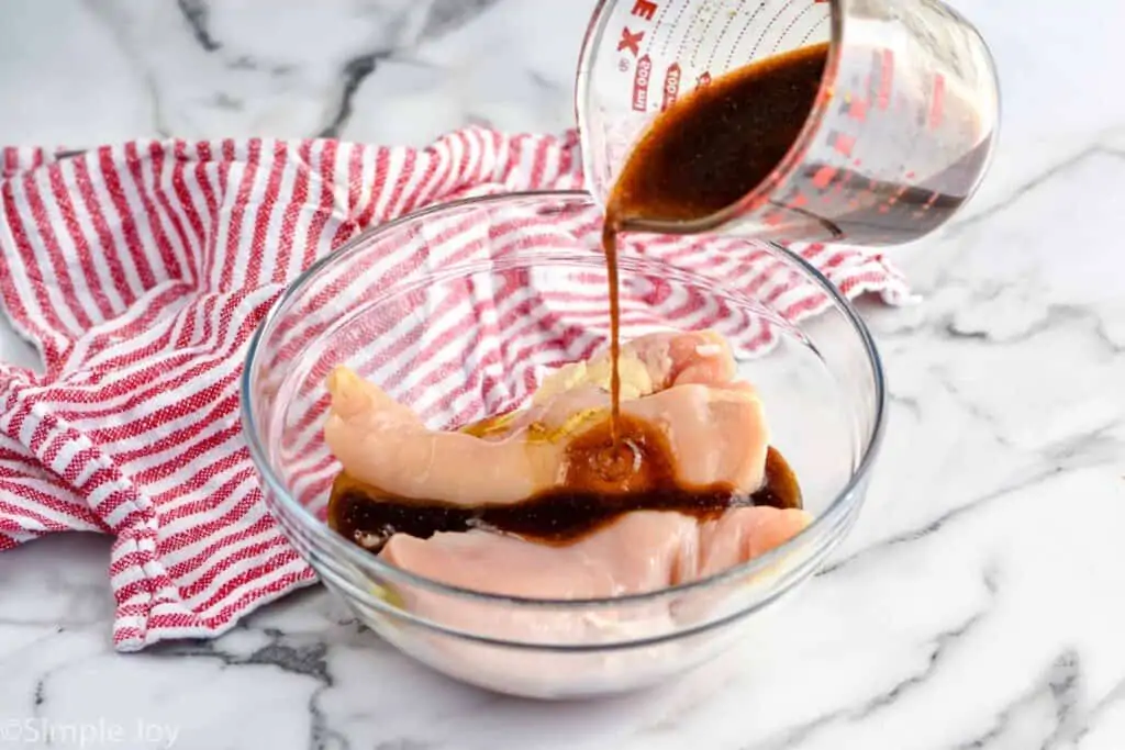 chicken marinade being poured over raw breasts in a bowl