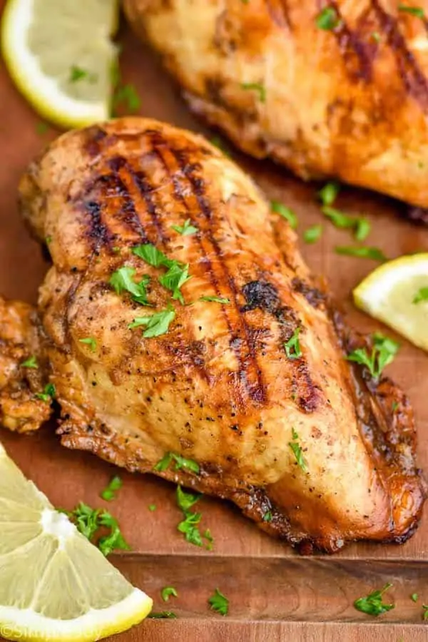 a chicken breast that has been marinated and then grilled on a cutting board garnished with parsley